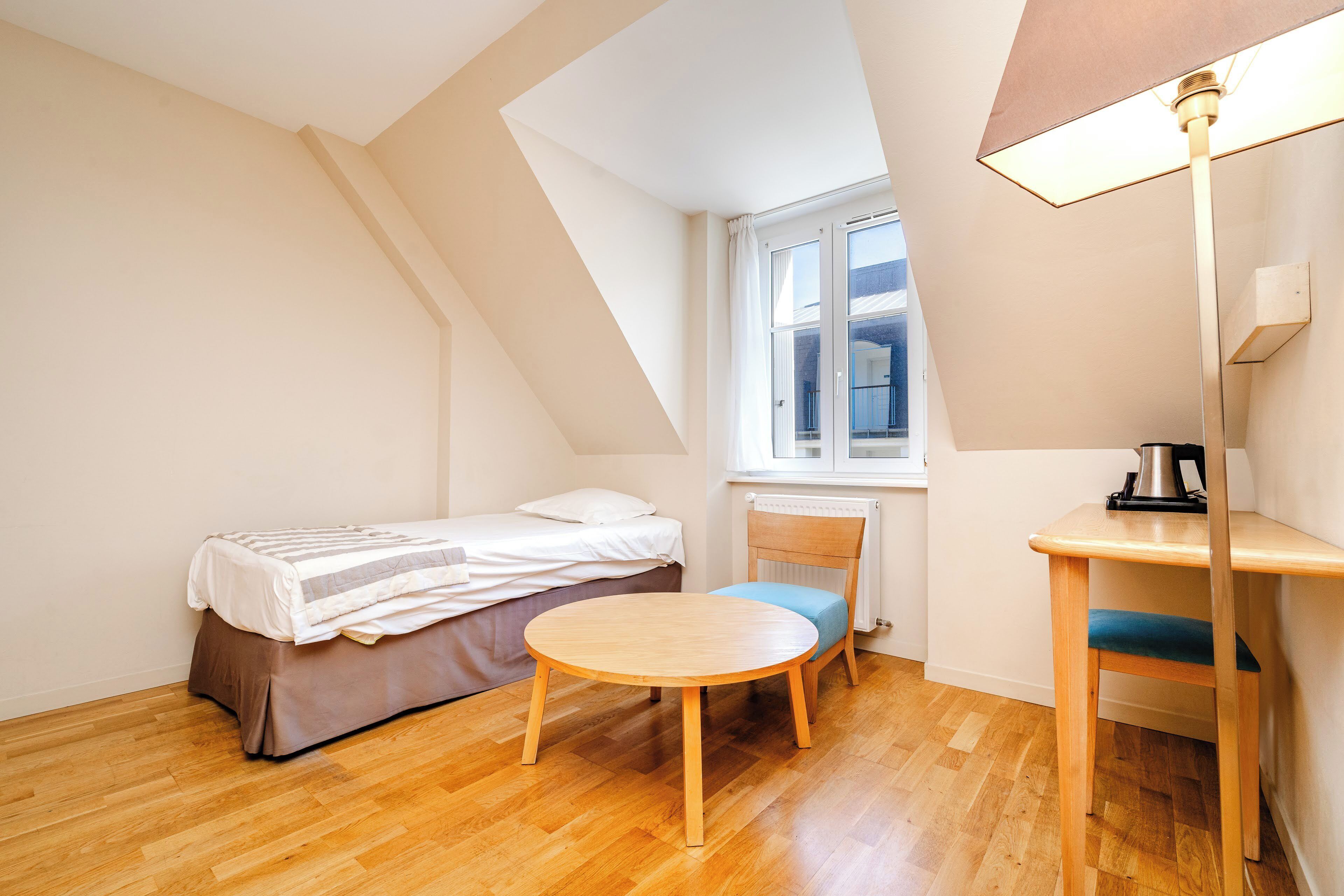 Una stanza piccola e luminosa con un letto, un tavolino rotondo e una sedia.