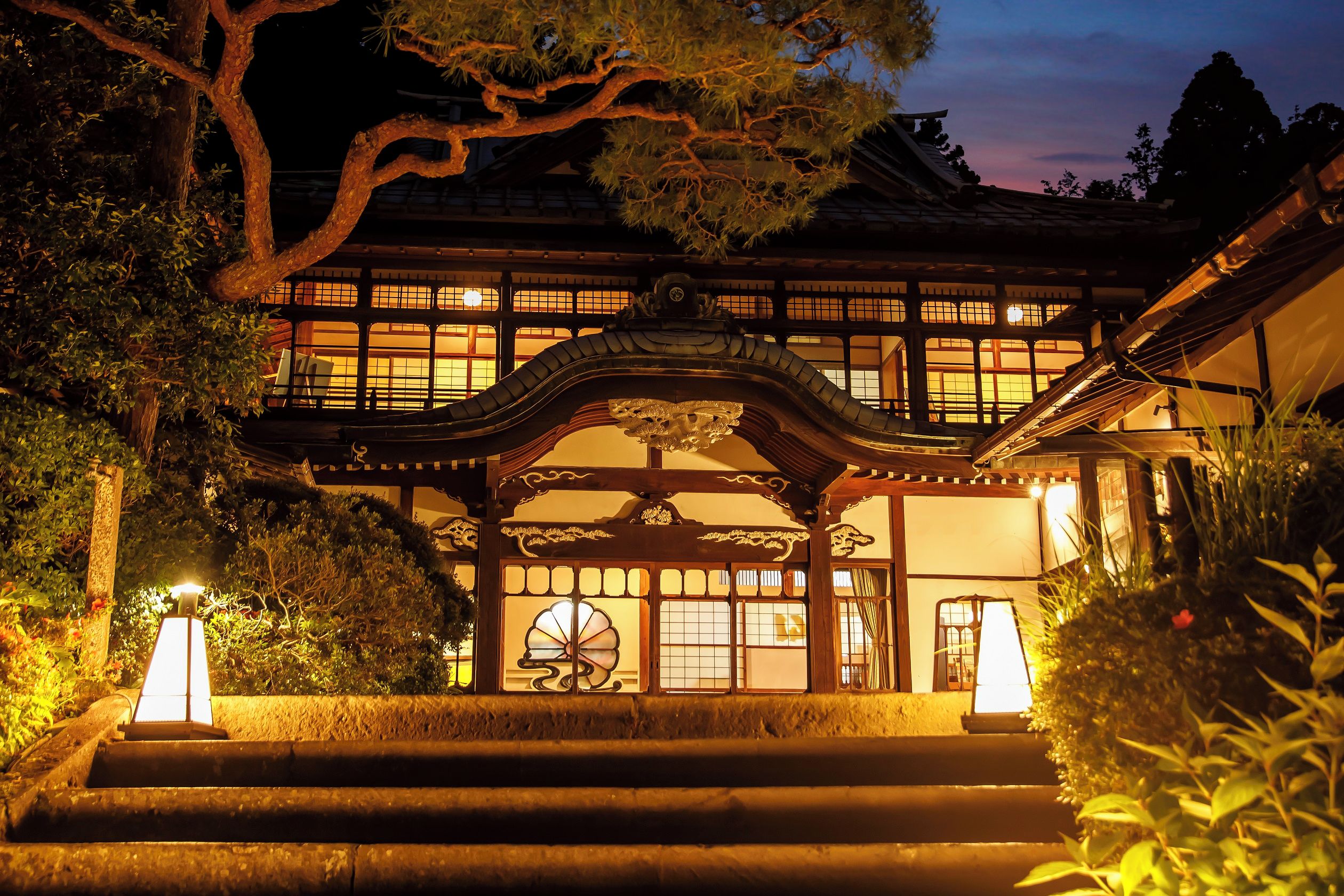 A traditional Japanese building with a wooden structure, a decorative entrance, and a staircase leading up to the entrance.