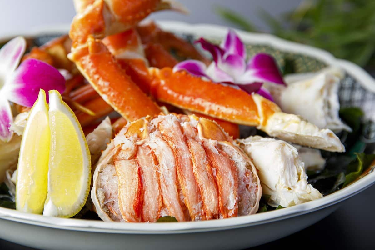 Un bol de mariscos, incluyendo patas de cangrejo y cola de langosta, adornado con limón y flores púrpuras.