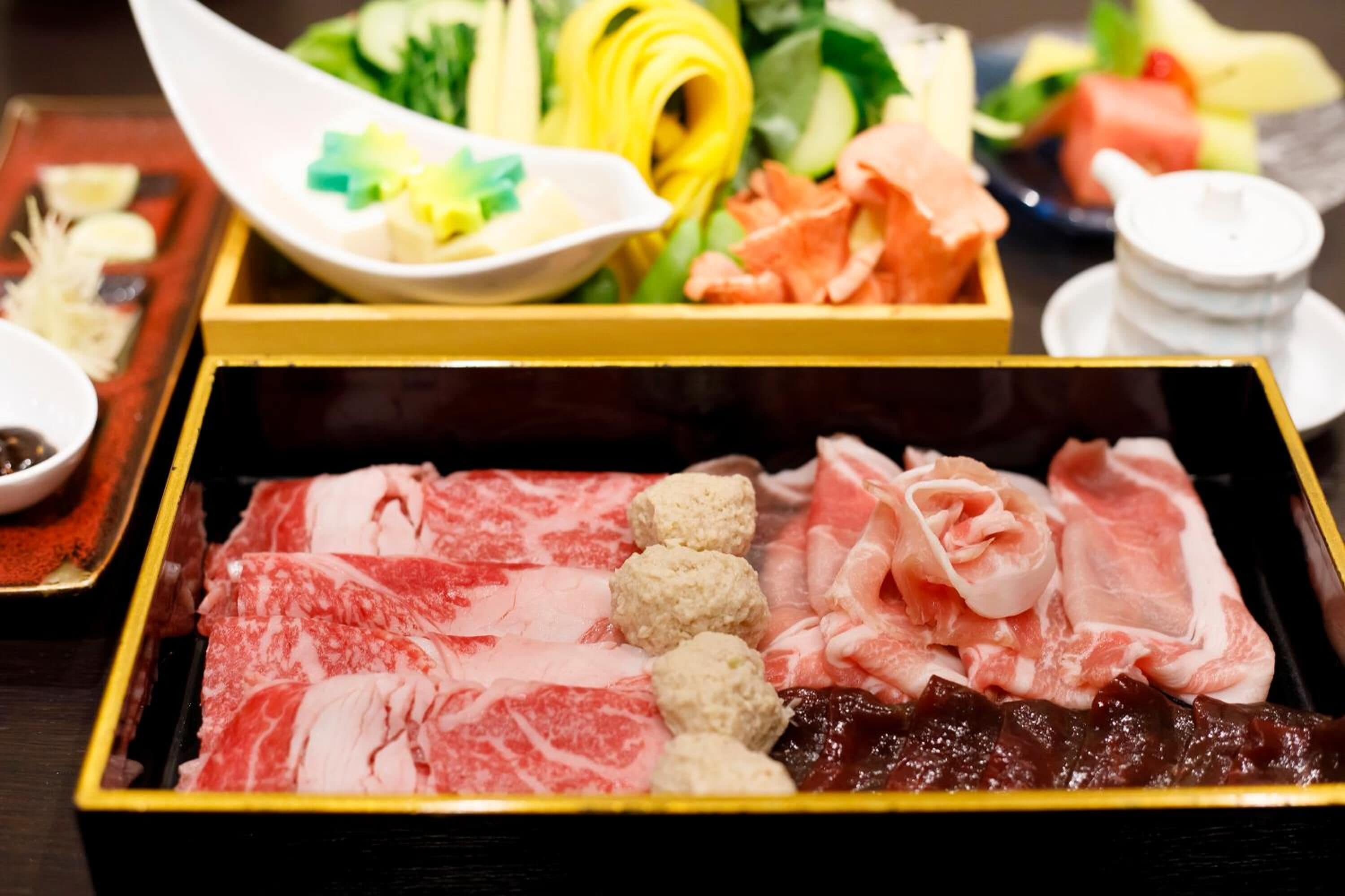 A variety of raw meats and vegetables on a tray, likely for a culinary experience.