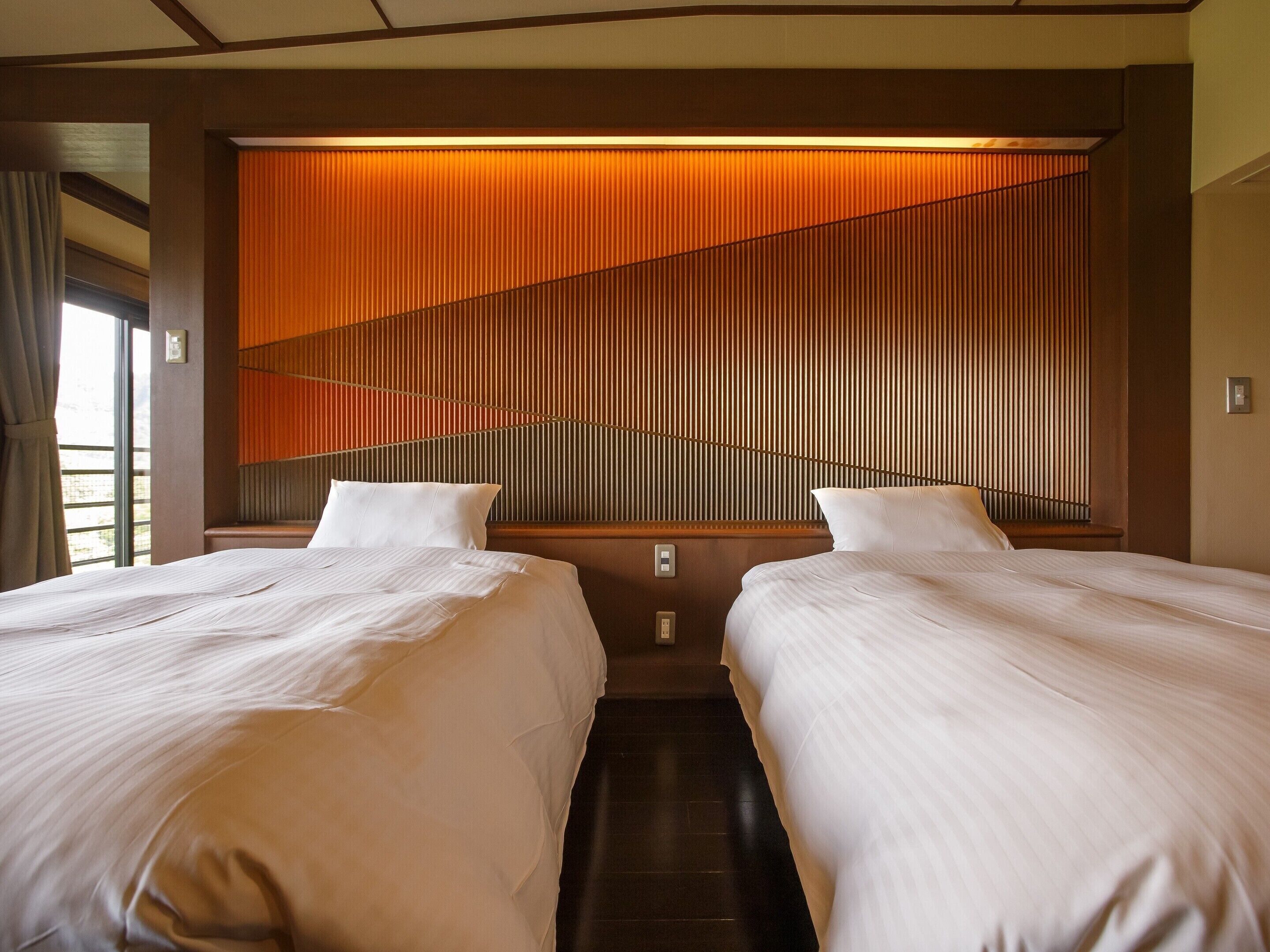 A hotel room with two beds, a wooden slatted headboard, and a window with curtains.
