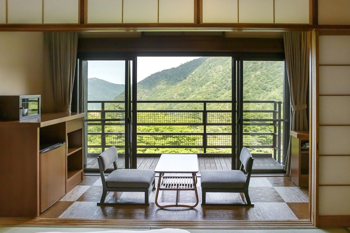 A room with a balcony, a table, two chairs, and a TV on a shelf.