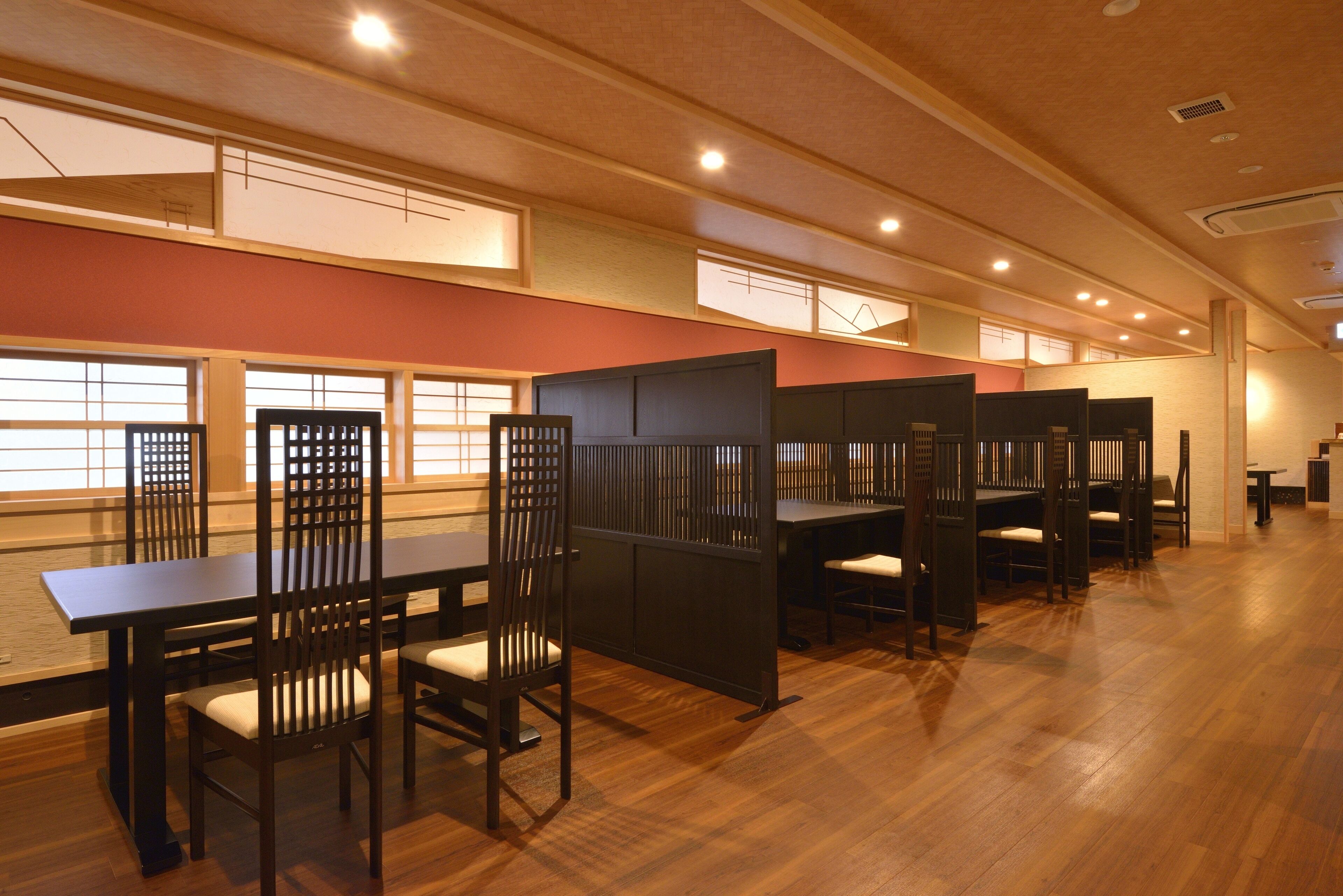 A spacious room with wooden flooring, multiple tables and chairs, and large windows allowing natural light.