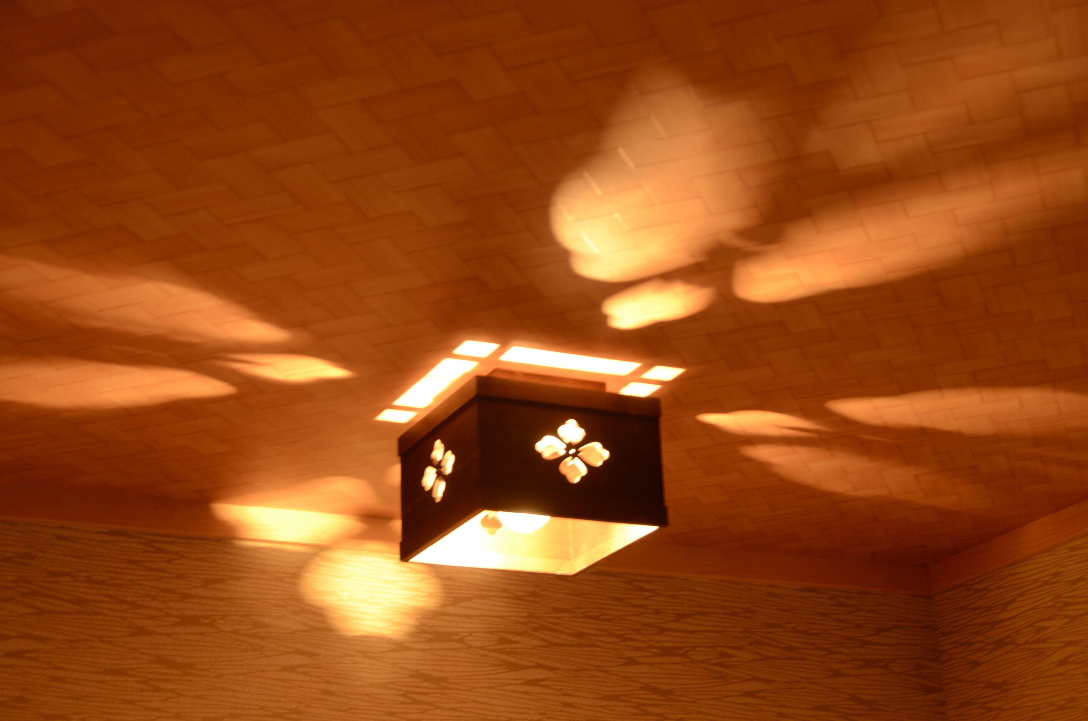A ceiling with a geometric light fixture casting shadows on a brick wall.
