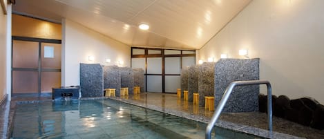 A modern indoor pool area with a clear water surface, stone walls, and a seating area with stools.
