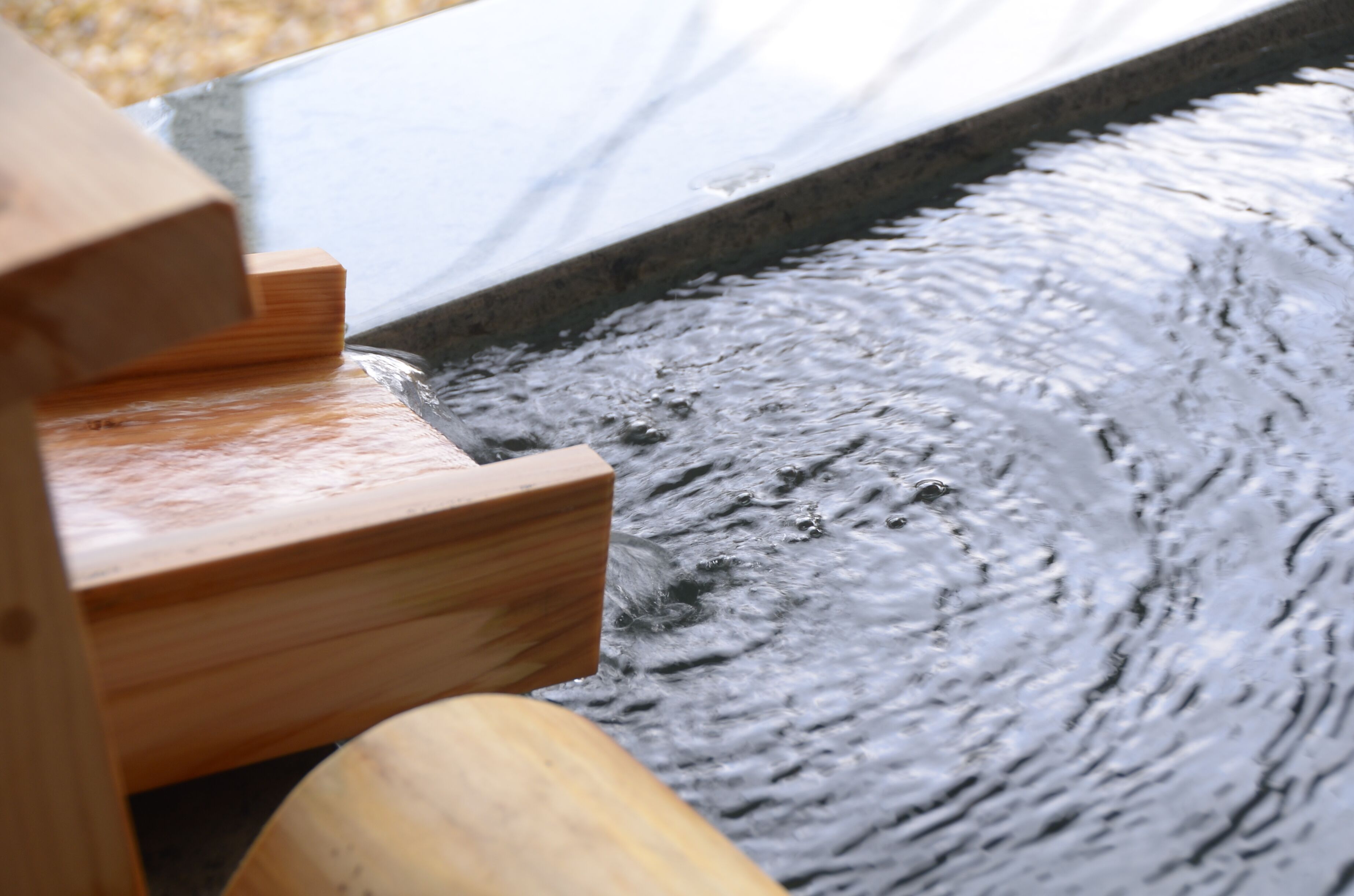 A wooden bench by a water feature with a stone edge.