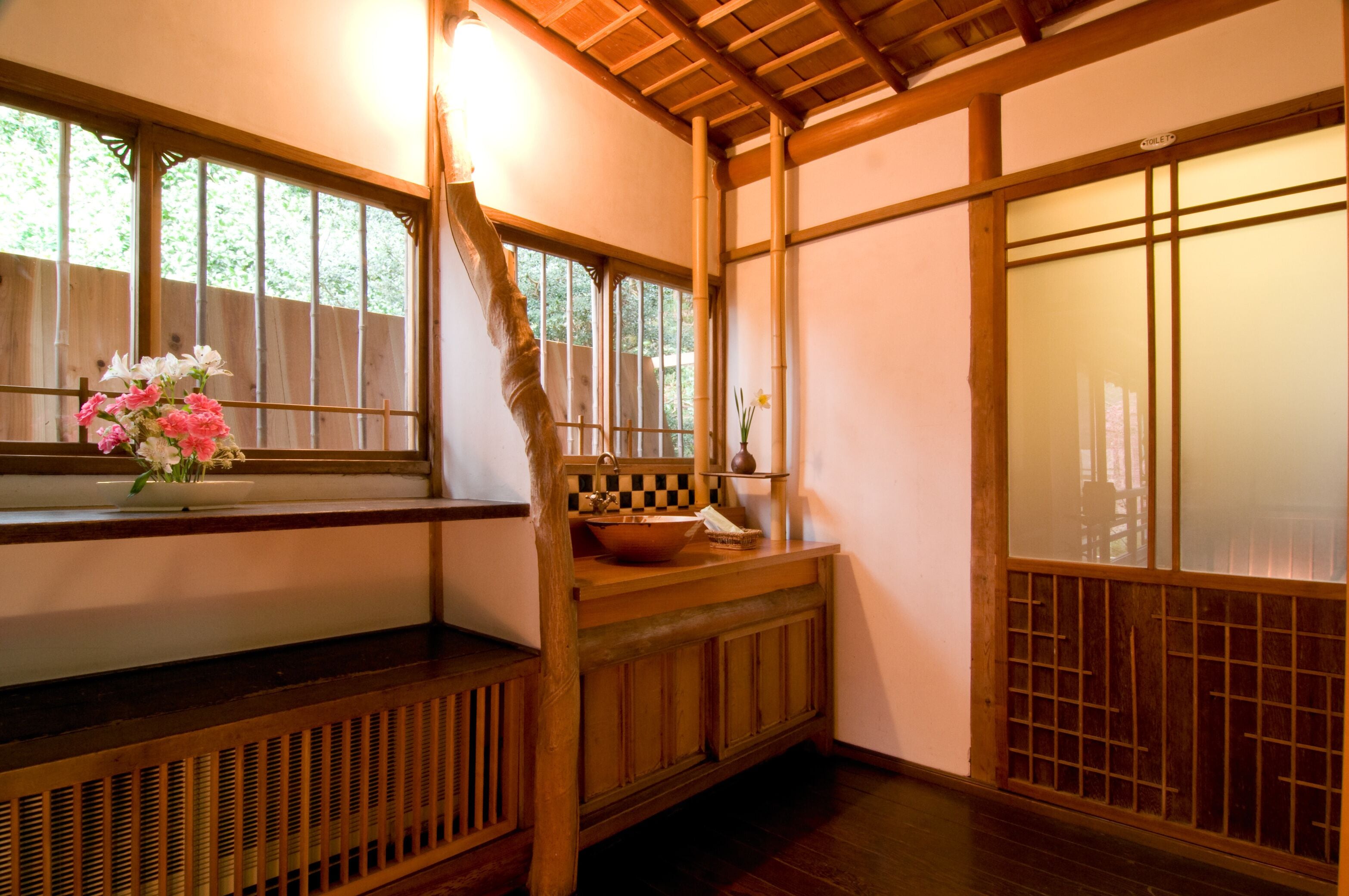 A traditional Japanese room with tatami flooring, a wooden bench, a window with a view of greenery, and a sliding door.