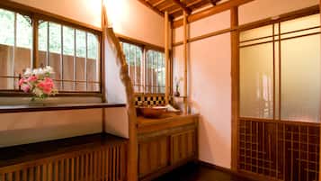 A traditional Japanese room with tatami flooring, a wooden bench, a window with a view of greenery, and a sliding door.