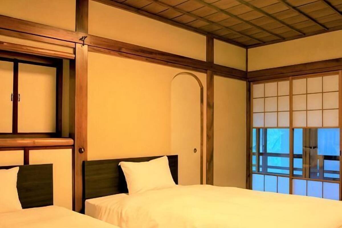 Habitación de hotel con dos camas, cabeceros de madera, un ventanal con vistas y puertas correderas tradicionales japonesas.