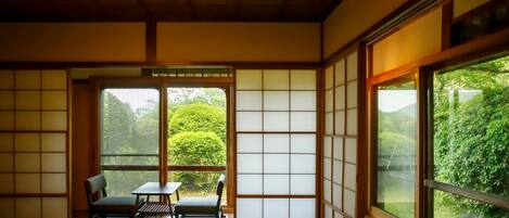 A traditional Japanese room with tatami flooring, sliding doors, and a view of greenery outside.
