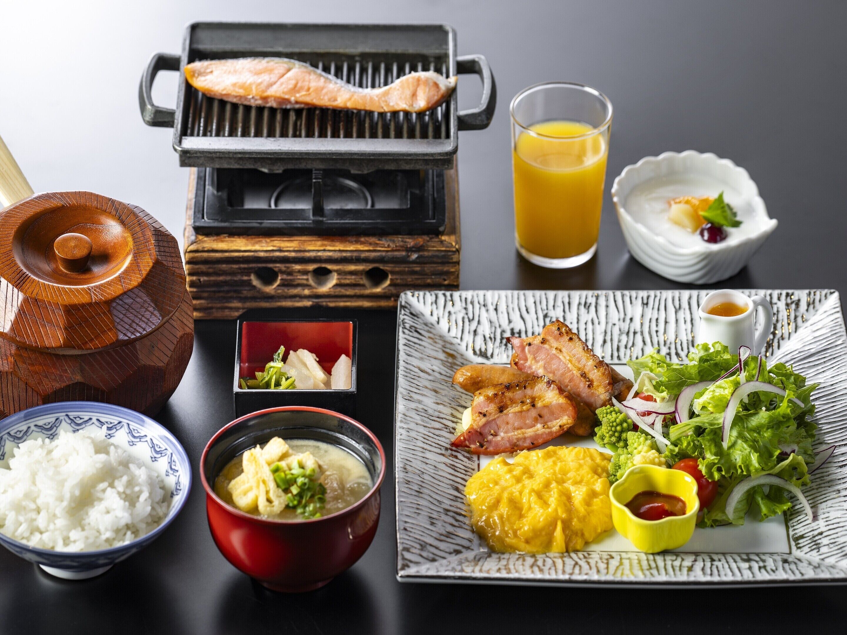 Variedad de platos japoneses, como pescado a la parrilla, arroz, sopa y una ensalada, acompañados de jugo de naranja.
