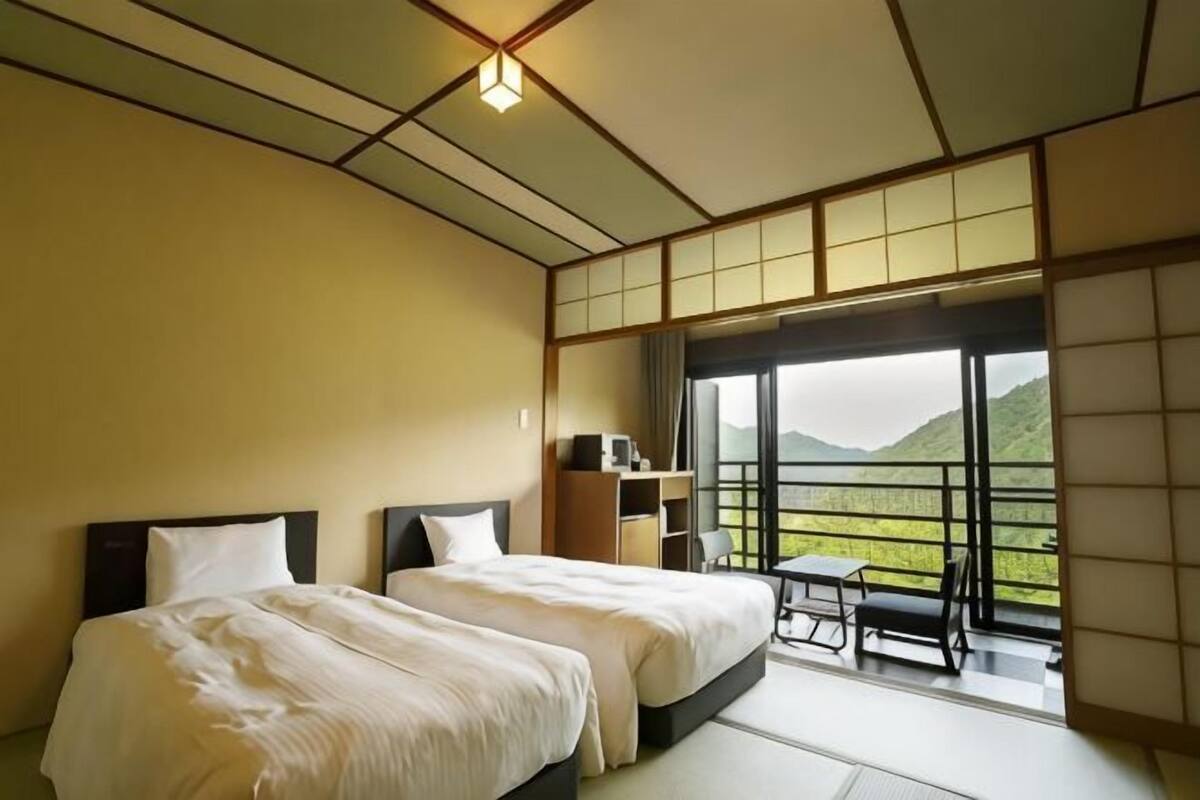 A hotel room with two beds, a desk, and a view of a mountainous landscape.