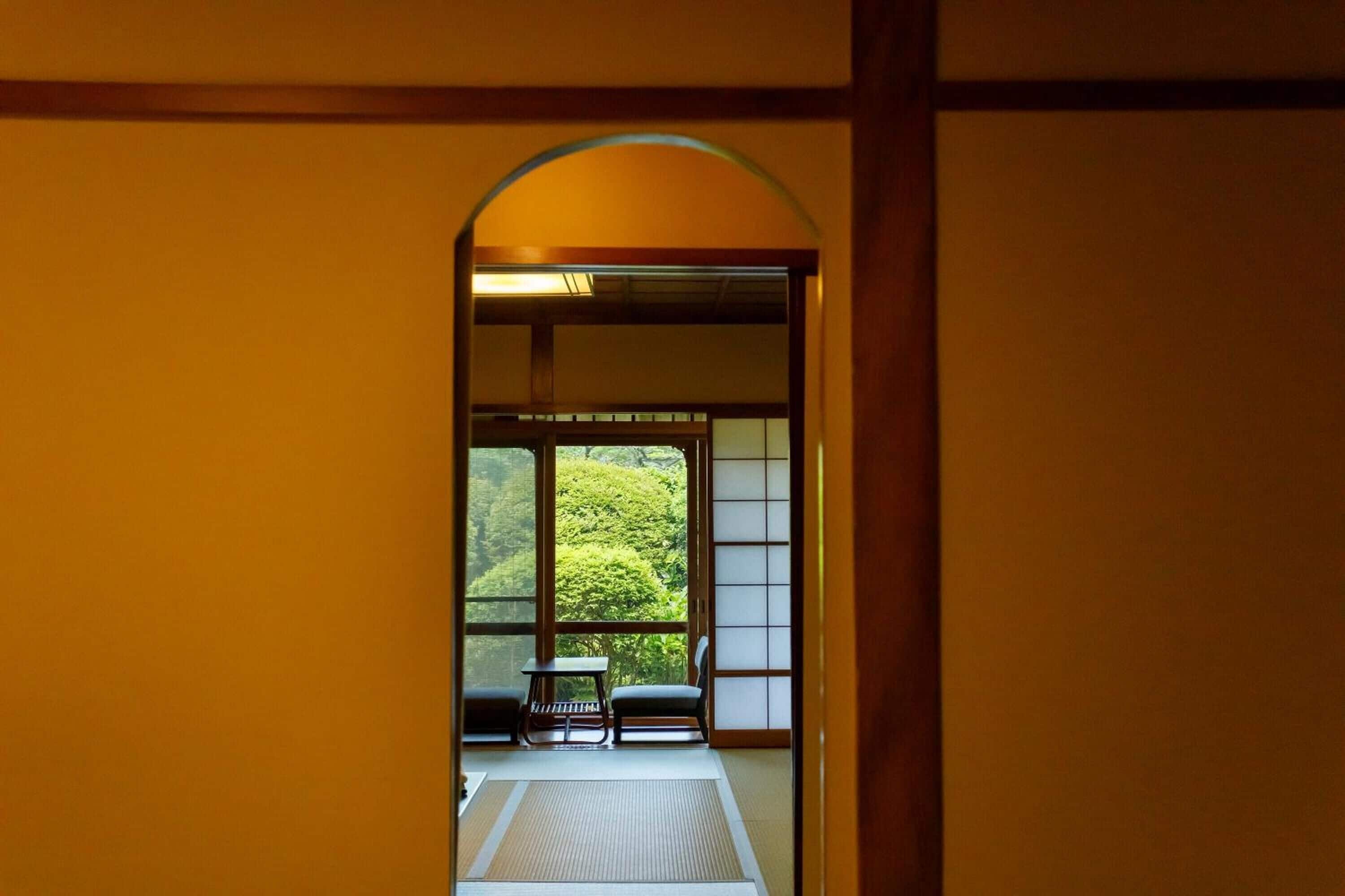 A traditional Japanese room with tatami flooring, a low table, and a view of lush greenery outside.