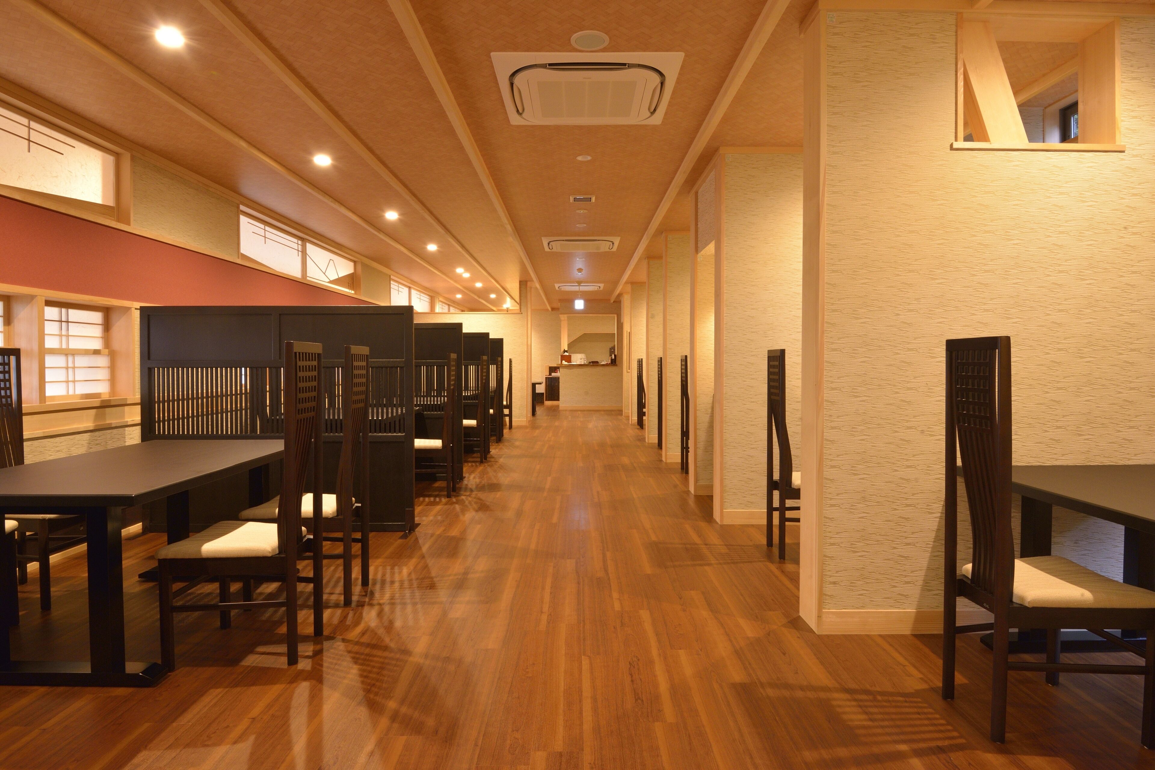A long corridor with multiple tables and chairs, wooden flooring, and recessed lighting.