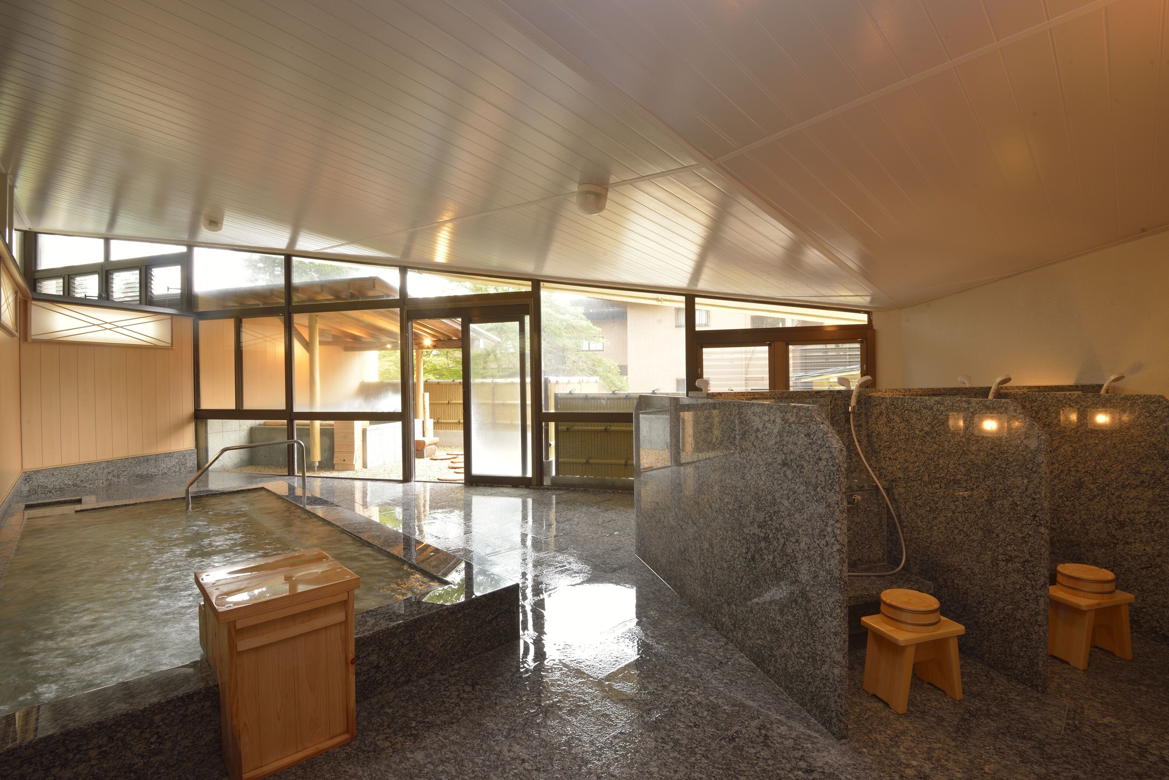 A modern indoor hot spring bath with a wooden cabinet, granite walls, and a glass door leading outside.