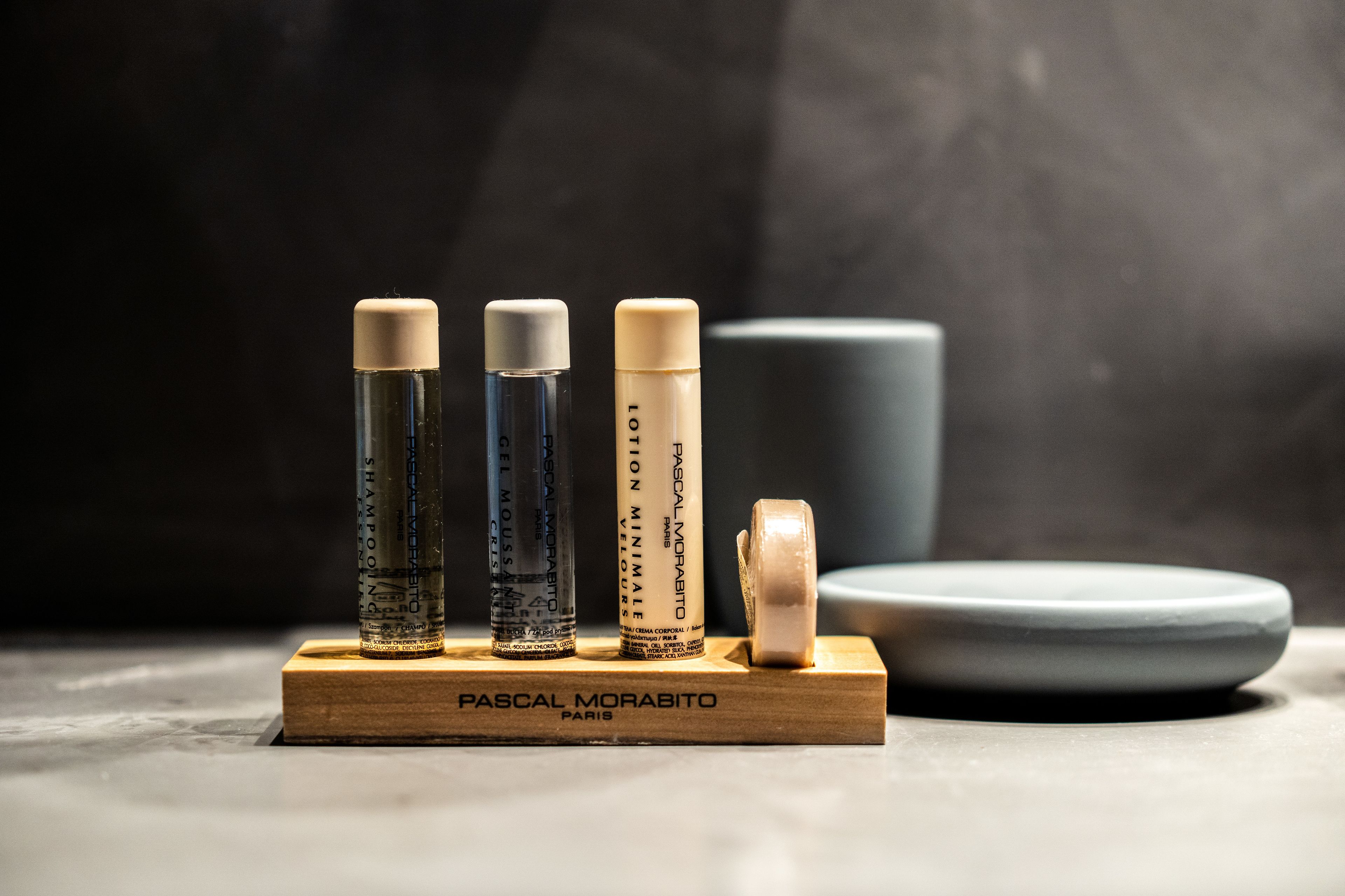 Four bottles of Pascal Morabito Paris hair products on a wooden stand with a plate and a cup in the background.