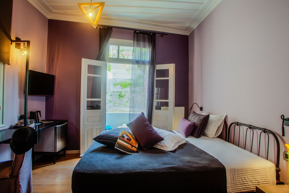 A bedroom with a bed, a desk, a chair, a TV, and a window with curtains.