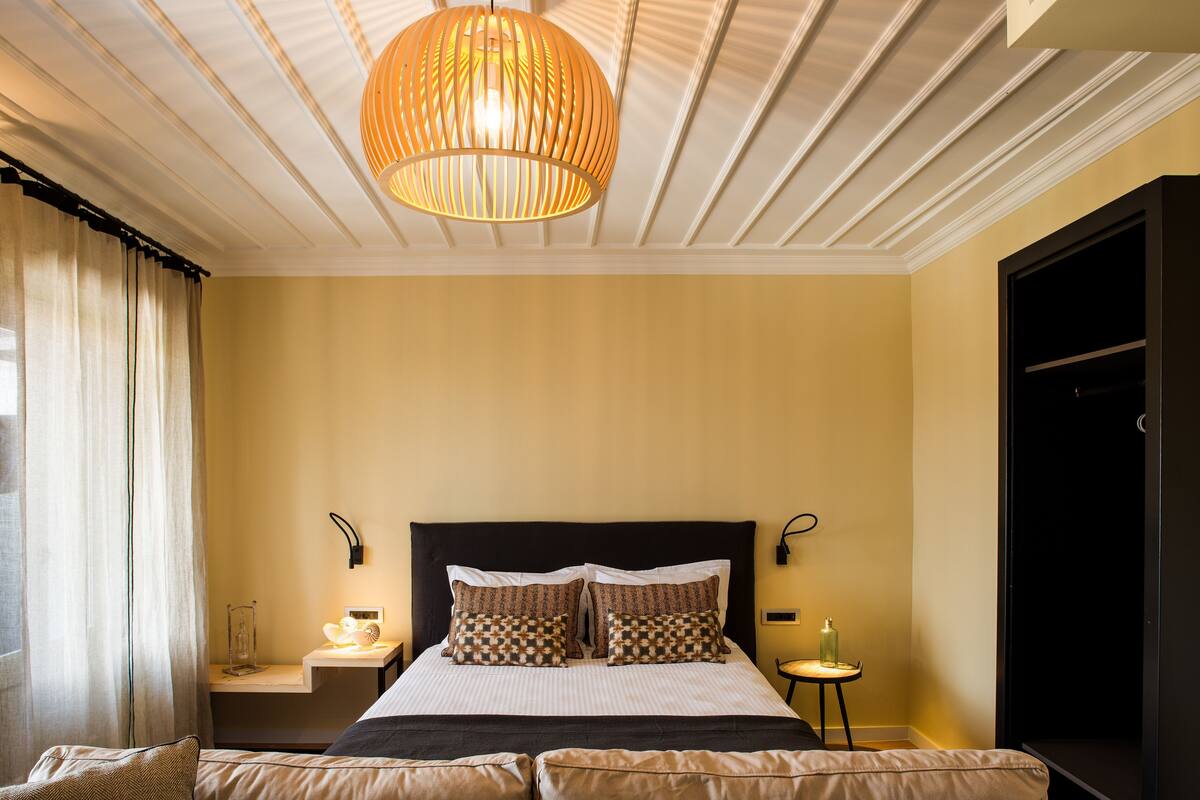 A neatly arranged bedroom with a large bed, bedside tables, a hanging light fixture, and a wardrobe.