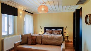 Une chambre à coucher comprenant un lit, un canapé, une table de chevet, une lampe, une fenêtre avec des rideaux et un radiateur.