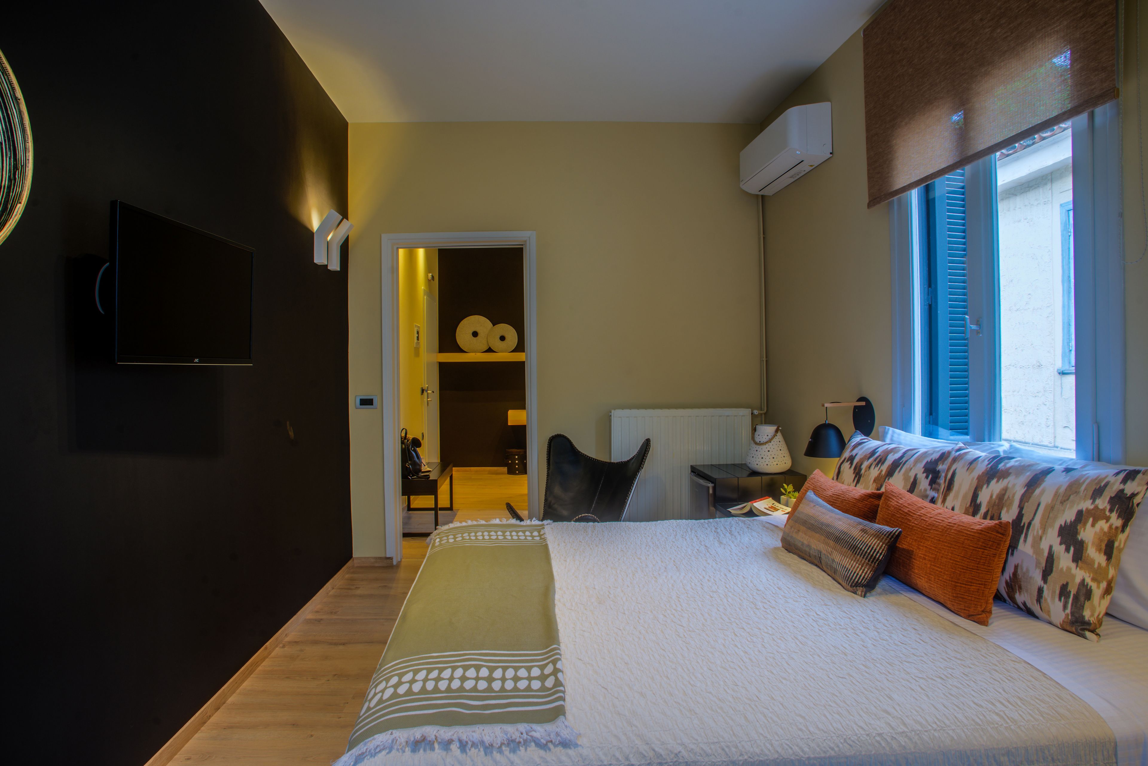 Un dormitorio con cama, televisor, escritorio con lámpara y ventana con persianas.