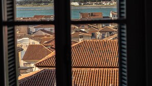 A window view of a coastal town with terracotta rooftops and a body of water. - Aethra Rooms (Nafplio)