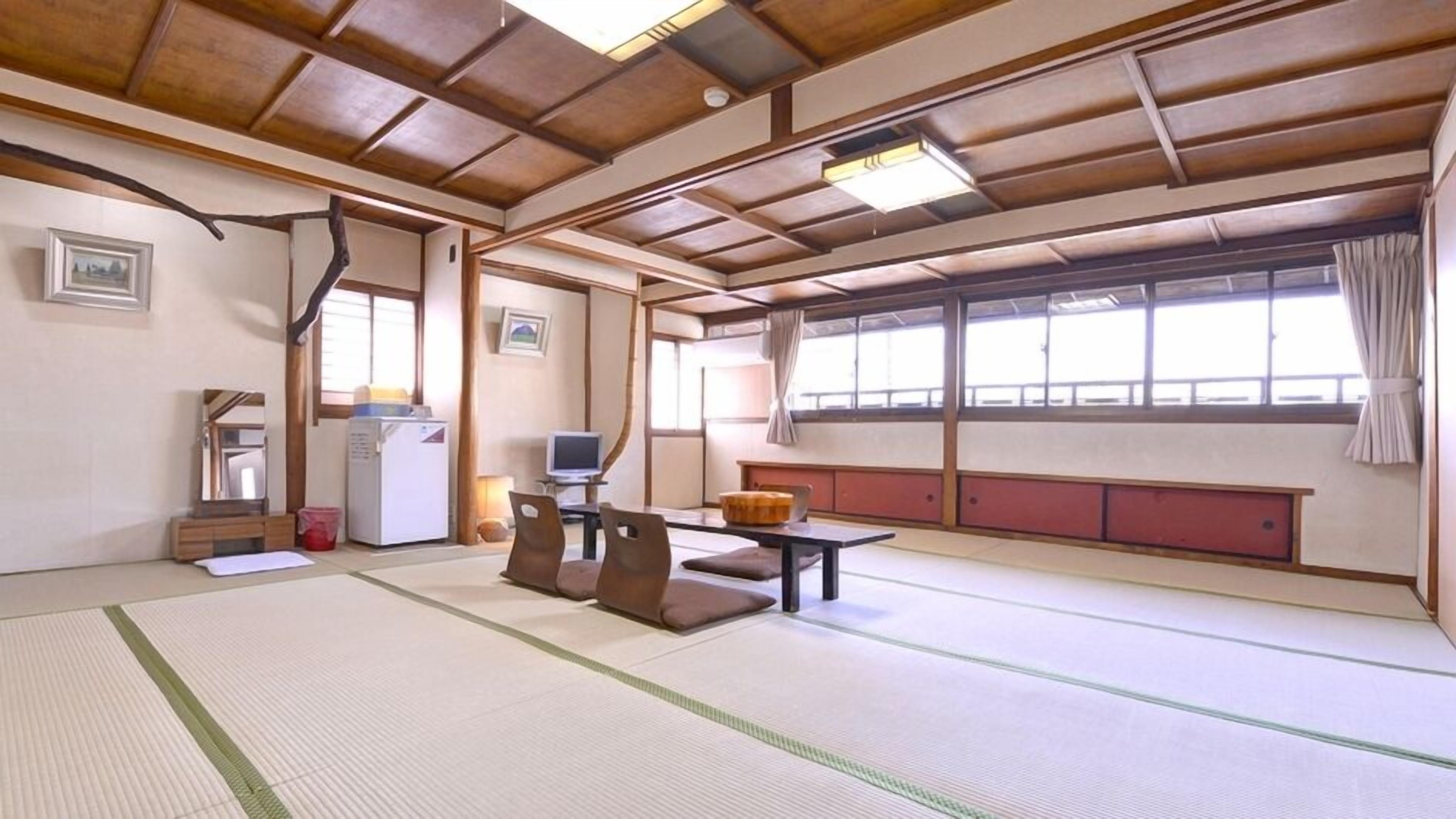Ein Zimmer mit Tatami-Matten, einem niedrigen Tisch, Kissen, einem Fernseher und einem Kühlschrank.