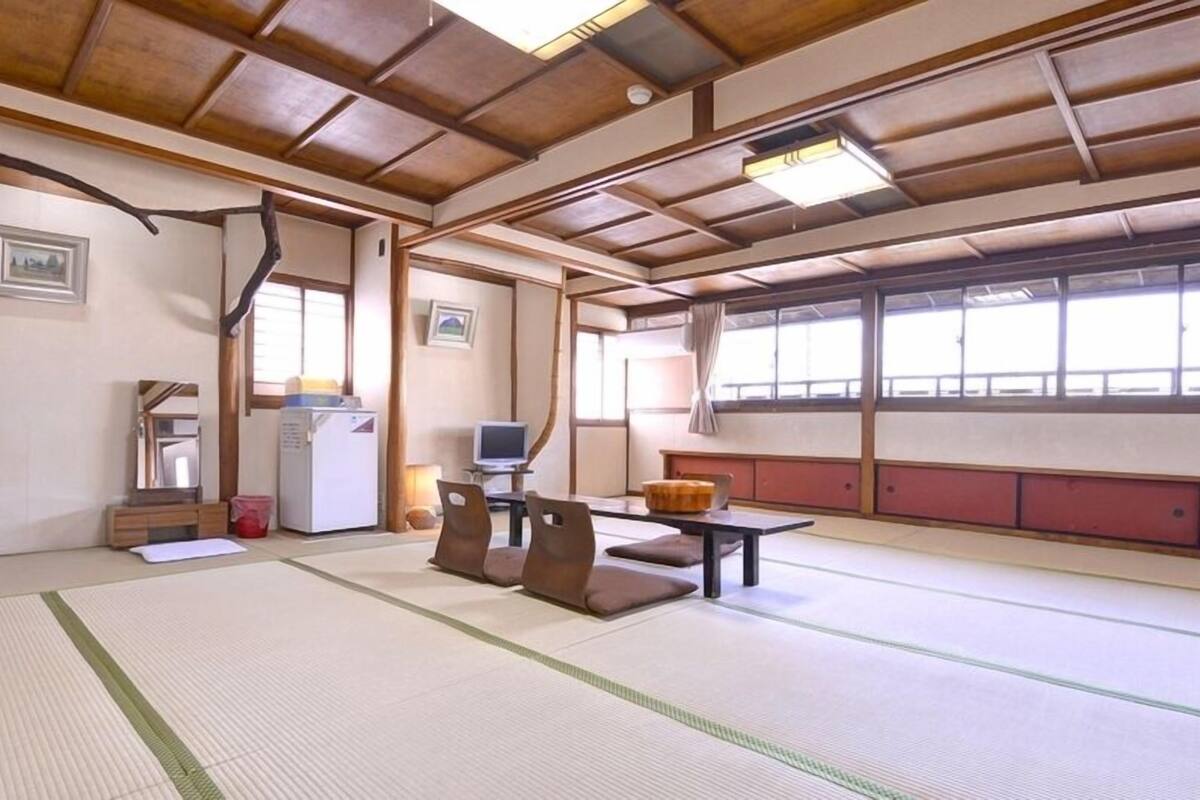 A tatami mat room with a low table, cushions, a television, and a refrigerator.