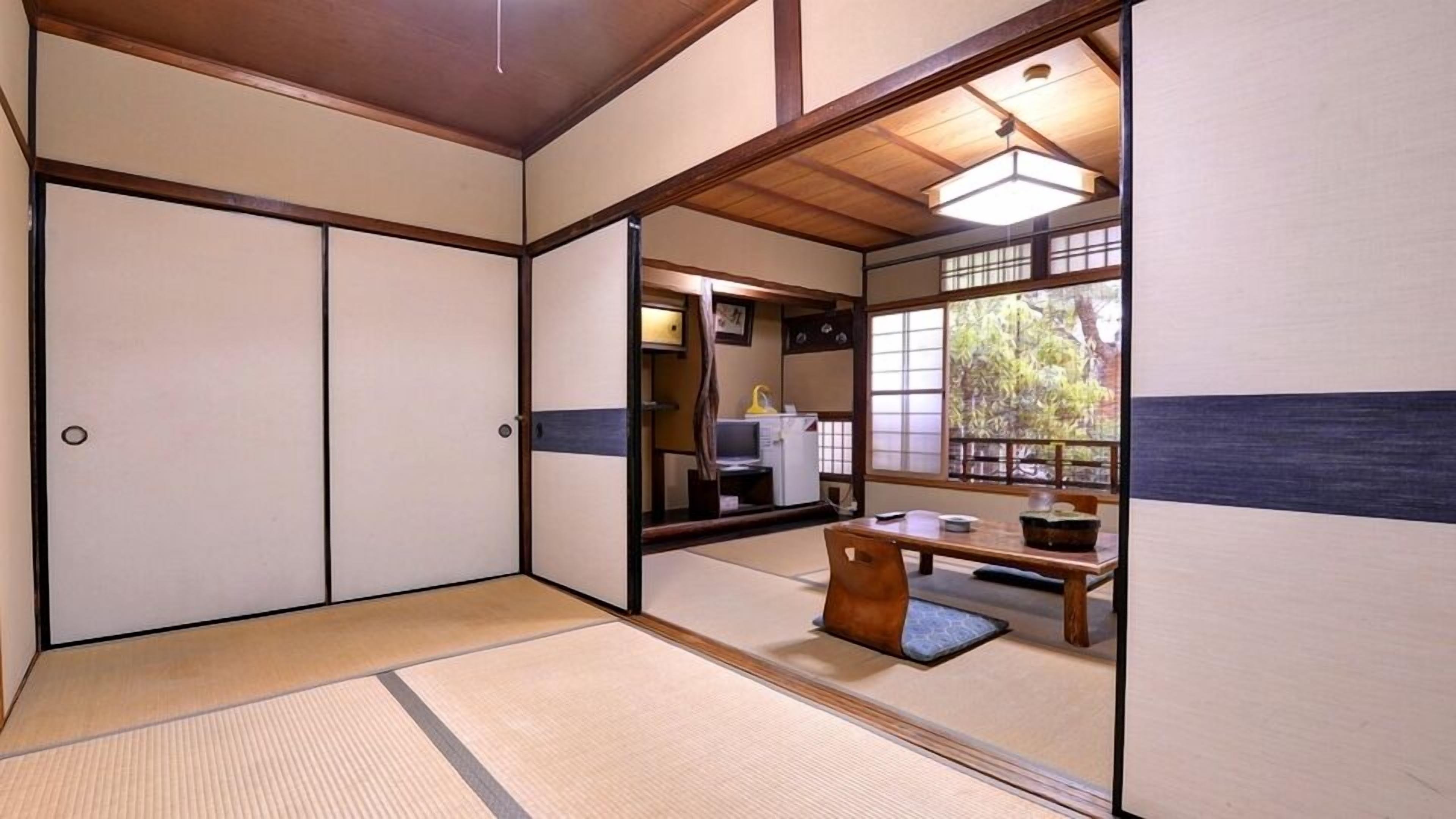 Ein traditioneller japanischer Raum mit Tatami-Böden, Schiebetüren, einem niedrigen Tisch mit Kissen und Blick ins Freie.