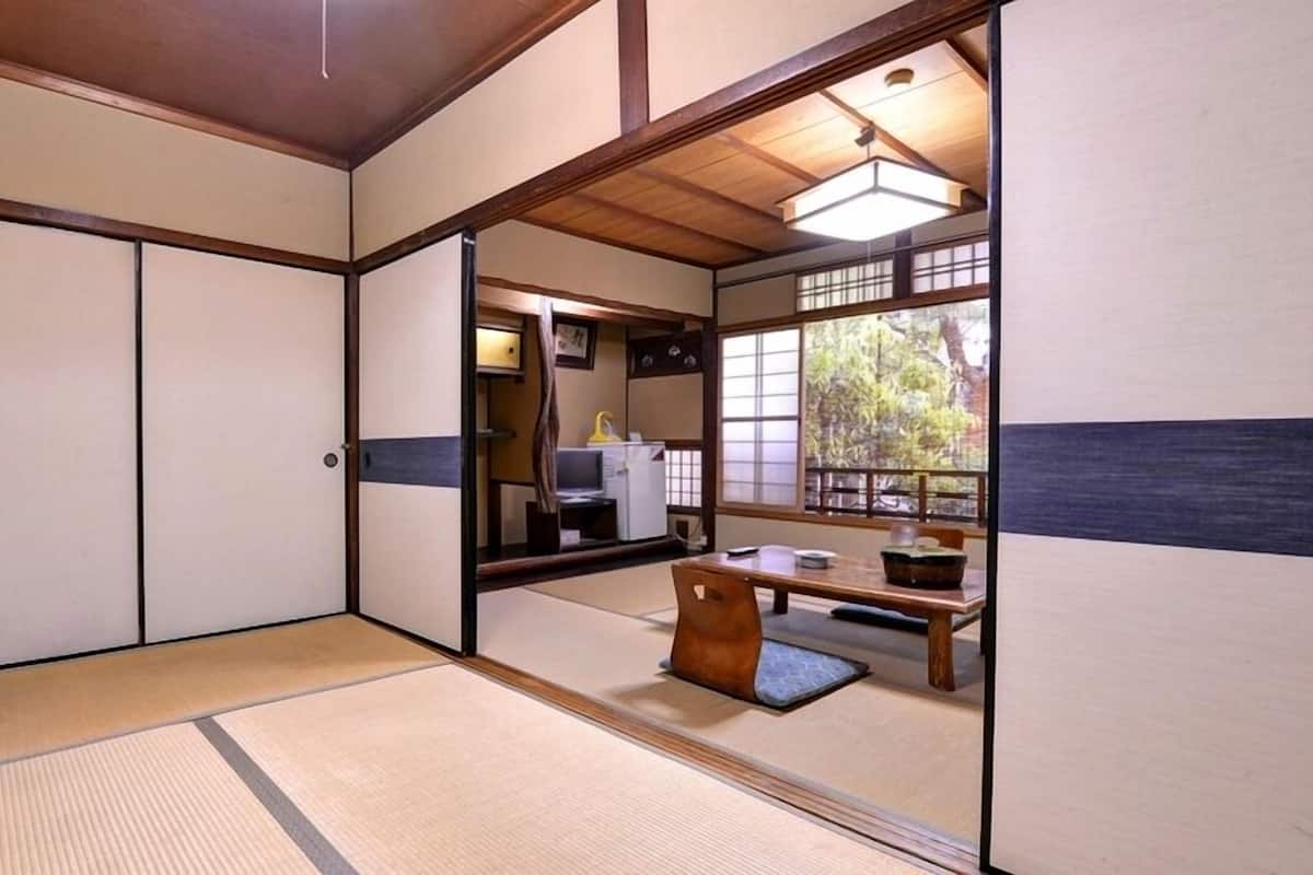 A traditional Japanese room with tatami flooring, sliding doors, a low table with a cushion, and a view of the outside.