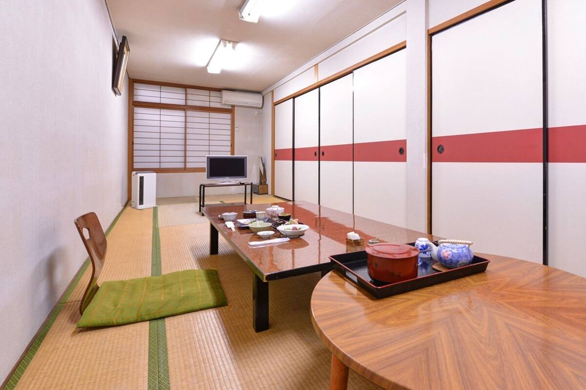 A traditional Japanese room with tatami flooring, a low table with dishes, a television, and sliding doors.