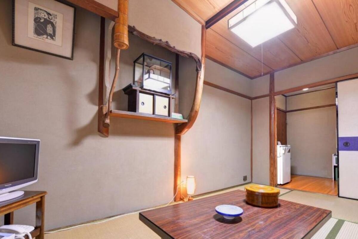 A traditional Japanese-style room with tatami flooring, a low wooden table, a television on a stand, and a shelf with storage boxes.