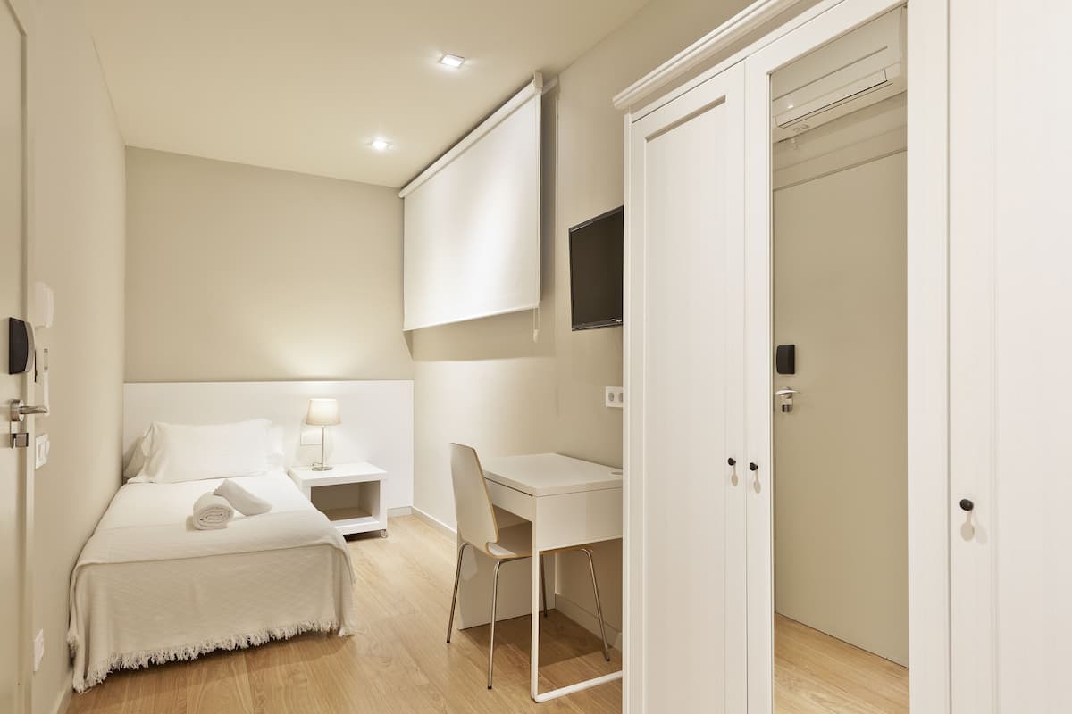 A hotel room with a bed, bedside table, chair, desk, and wardrobe.