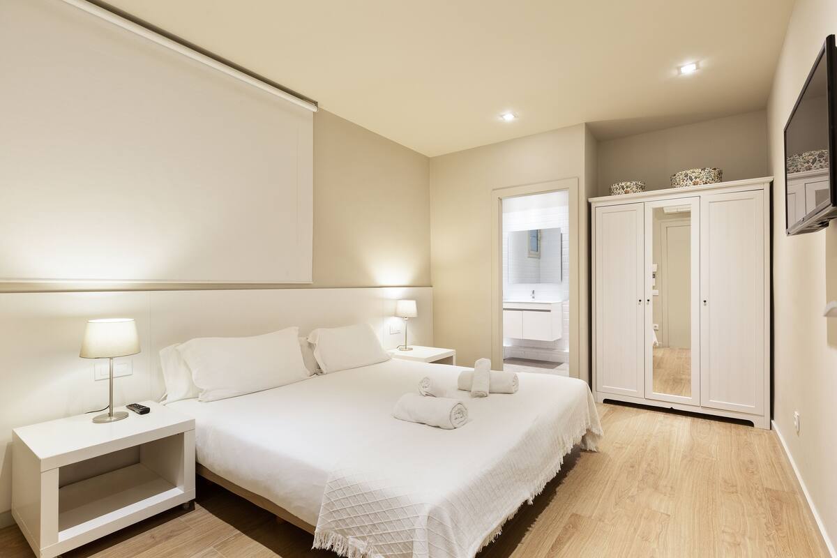A neatly arranged bedroom with a bed, bedside tables, a wardrobe, and a television.