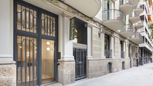 A building facade with a large glass entrance, a sign reading "ola living," and multiple balconies with metal railings. - Ola Living Hostal Diagonal (Barcelona)
