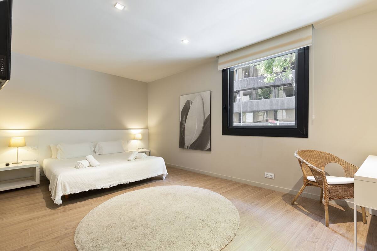 A bedroom with a bed, bedside tables, a chair, a large window, and a wall-mounted artwork.
