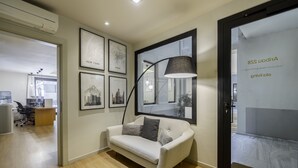 A modern office space with a white sofa, framed cityscape pictures, and a large mirror. - Ola Living Hostal Diagonal (Barcelona)