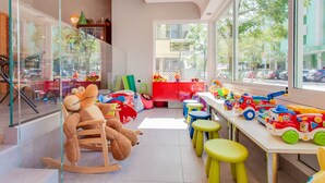 Una sala de juegos infantil con una mecedora, taburetes de colores y vehículos de juguete.