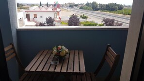 Un balcón con mesa y sillas de madera, un florero con flores y vistas a una autopista y edificios.
