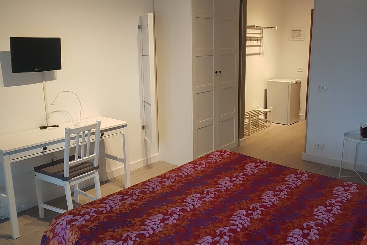 A bedroom with a bed, a desk, a chair, a TV, and a wardrobe.