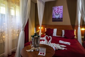 Quarto de hotel com cama, mesa de cabeceira com uma garrafa de champanhe, duas taças e arranjo de toalha em formato de coração.