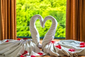 A room with a view of greenery through a window, a heart-shaped towel arrangement, and a bed with white linens and red rose petals. - Patak Park Hotel (Visegrád)