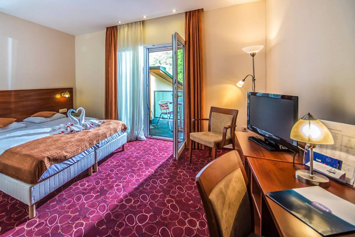 A hotel room with a bed, a desk with a computer, a chair, and a television.