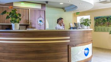 A reception desk with a wooden finish, a neon sign, and a large plant.