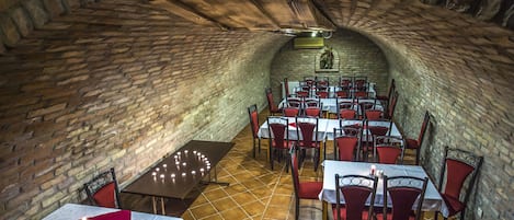 A restaurant with brick walls and a vaulted ceiling, featuring tables and chairs arranged for dining.