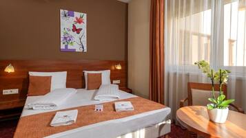 A hotel room with a large bed, two bedside tables, a small table with a plant, and a painting on the wall.