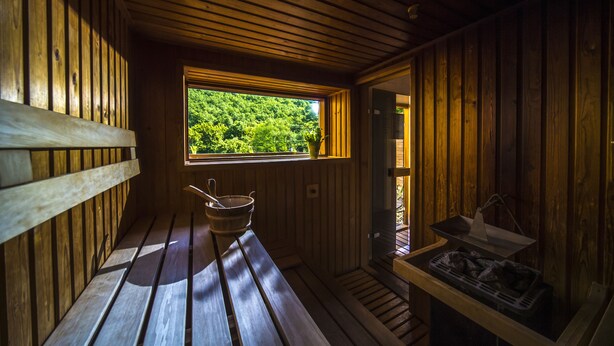 Puisesta laudelavasta ja ikkunasta, josta avautuu näkymä vehreään maisemaan, koostuva sauna. Oikealla puolella on tarjotin, jossa on erilaisia esineitä.