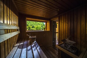 A wooden sauna with a bench, a window with a view of greenery, and a tray with items on the right side. - Patak Park Hotel (Visegrád)
