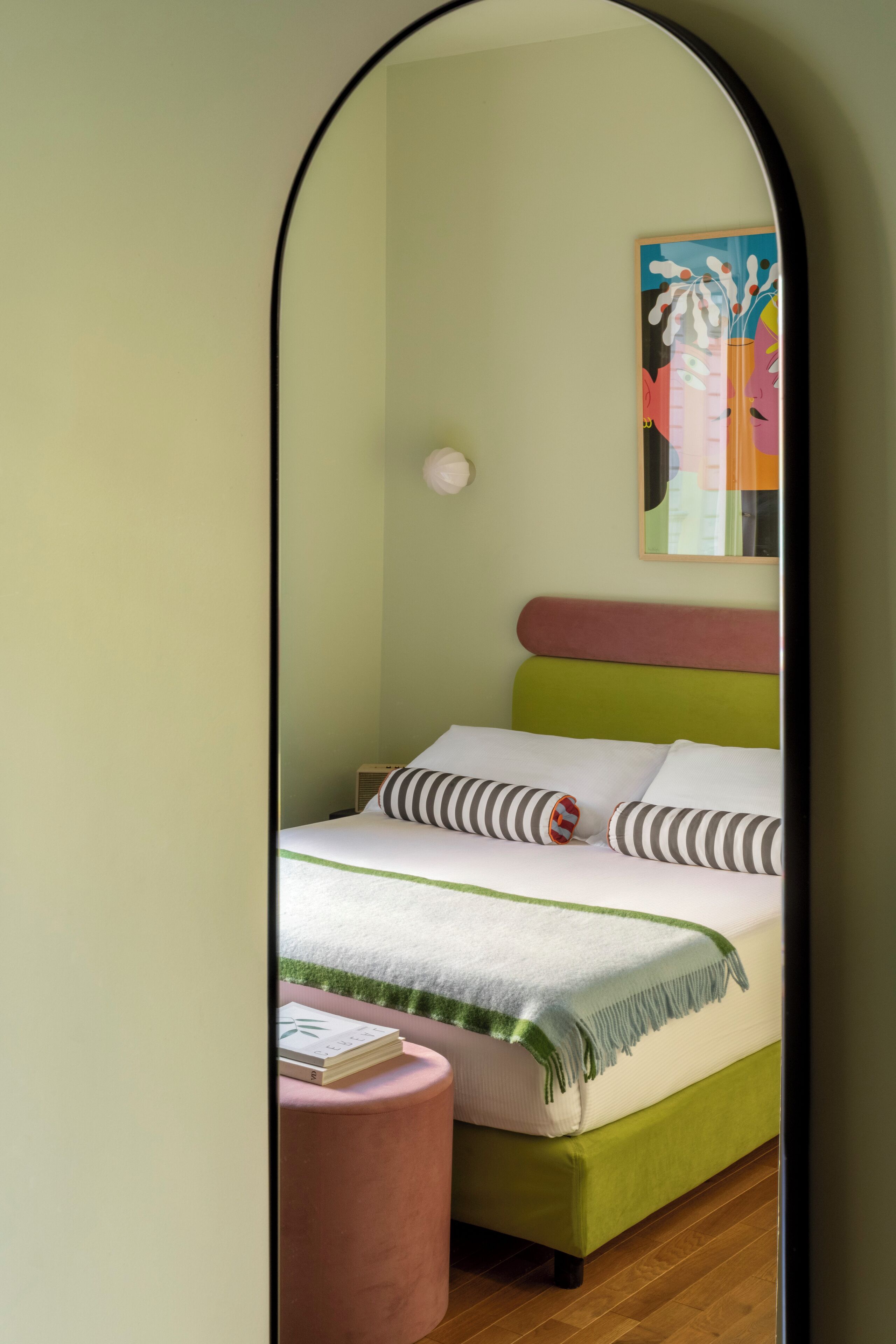 A bedroom with a bed, a bedside table, a mirror, and a painting on the wall.