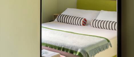 A bedroom with a bed, a bedside table, a mirror, and a painting on the wall.