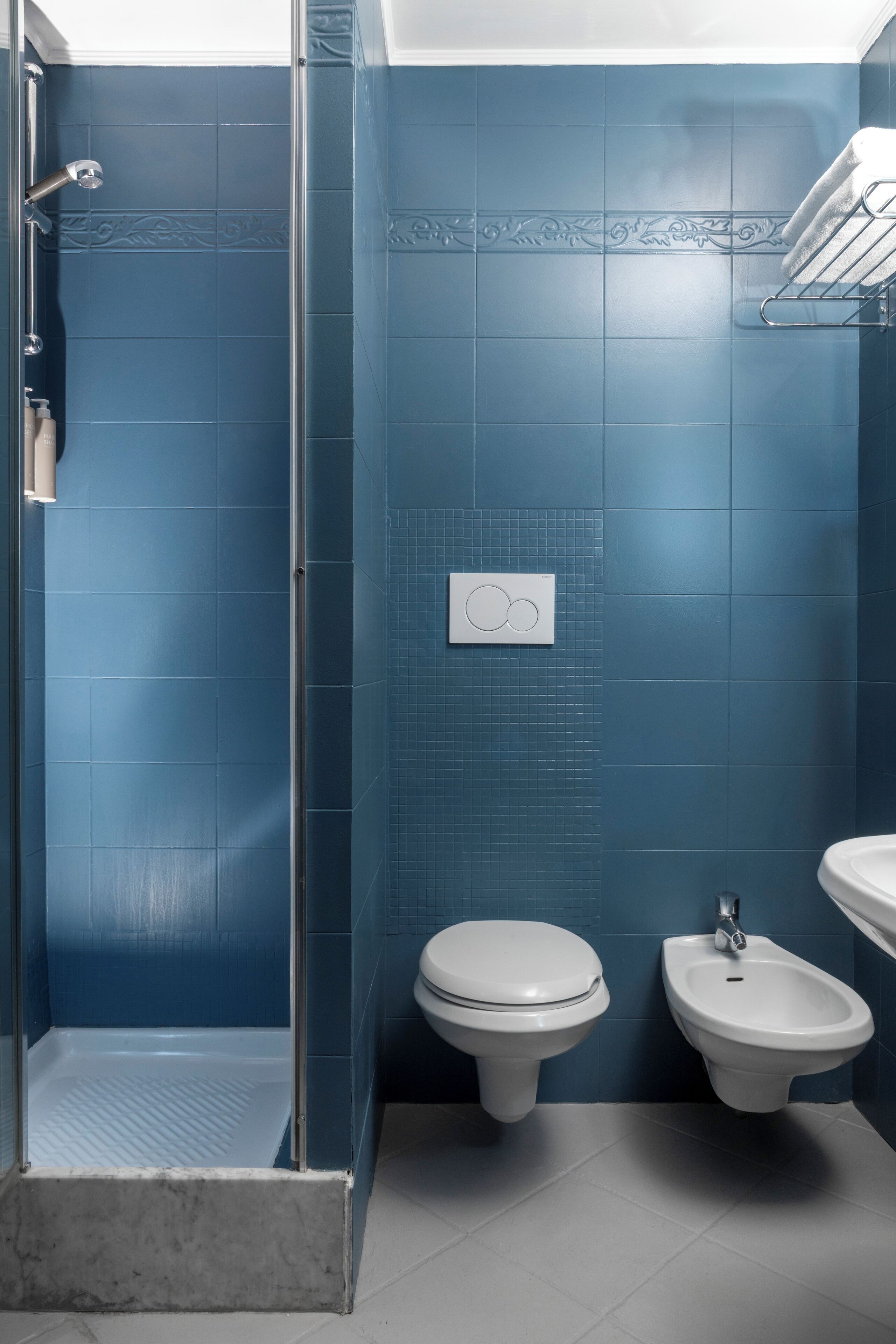 A bathroom with blue tiles, a glass shower enclosure, a toilet, and a bidet.